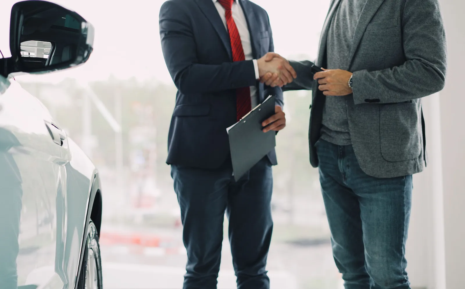 Two men shaking hands across a desk inside a car dealership showroom