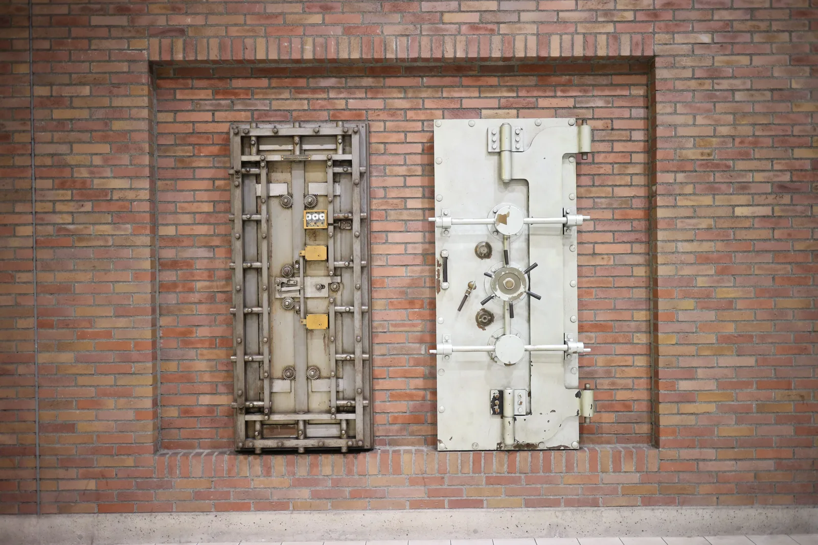 Two heavy steel bank vault doors mounted in a brick wall