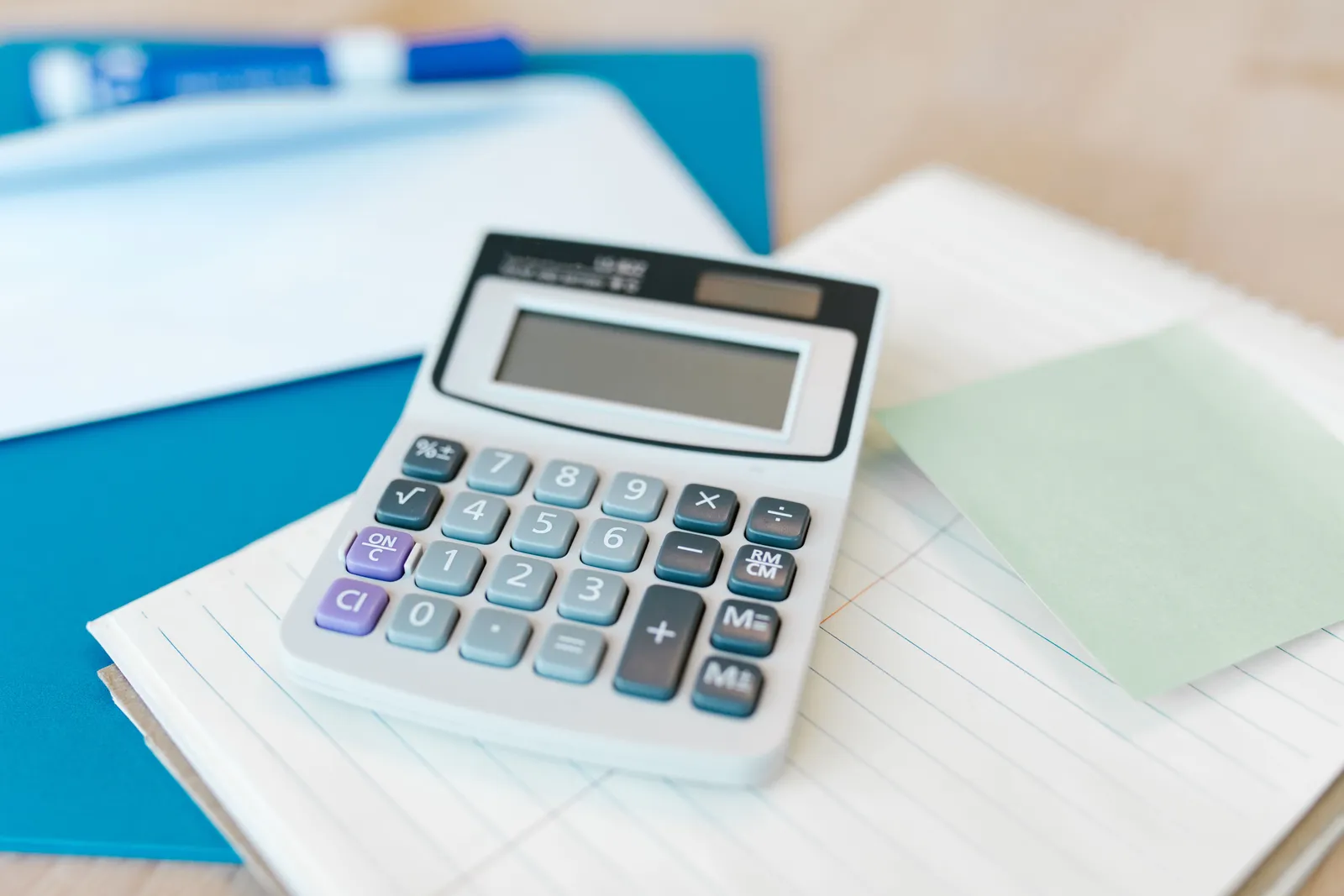 Calculator resting on a lined notepad beside a blue folder on a desk