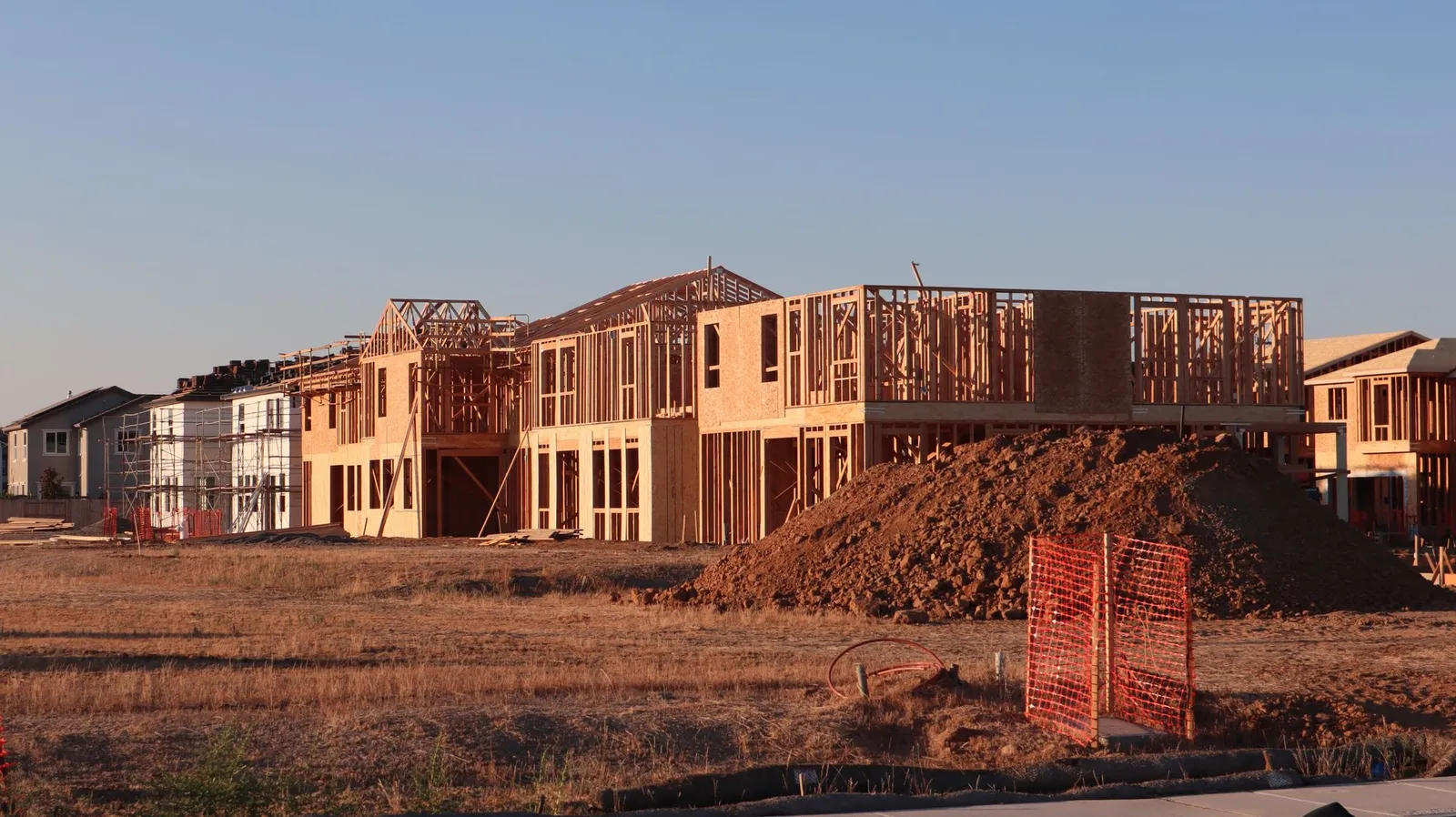 Wood-framed new houses under construction beside a dirt pile at sunset