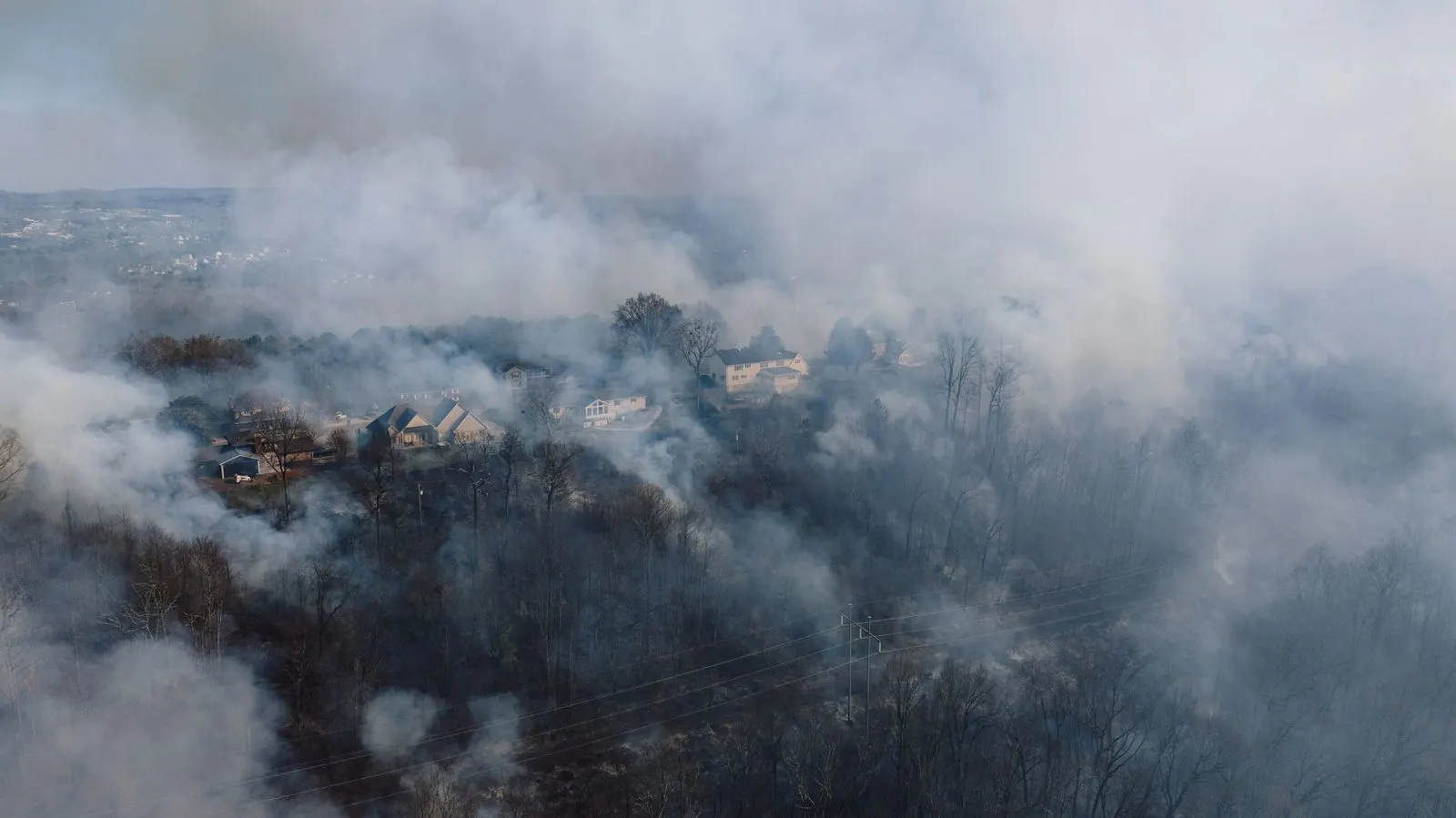Houses on a wooded hillside surrounded by thick gray wildfire smoke
