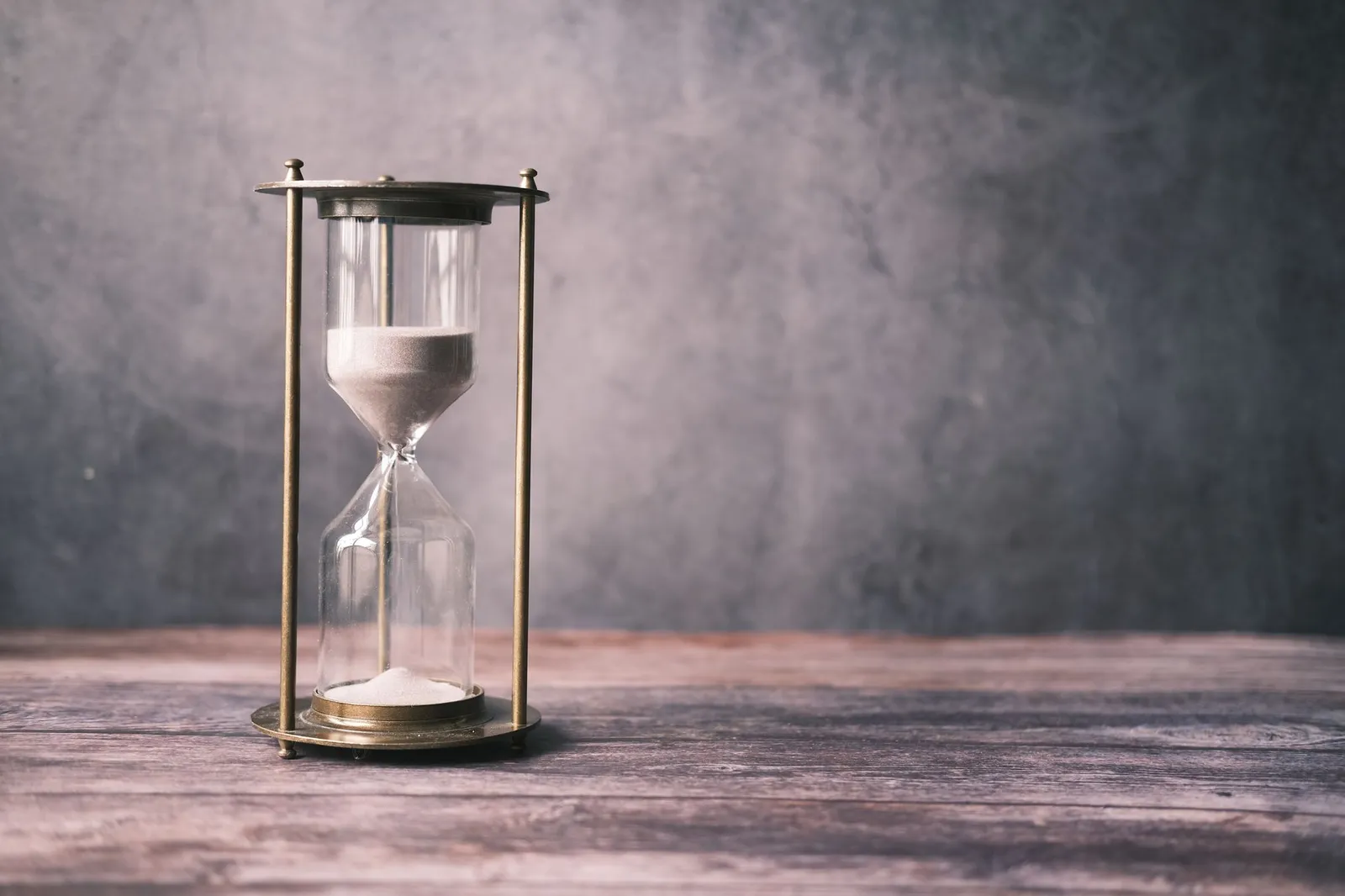 Hourglass with sand on a wooden table against a gray background