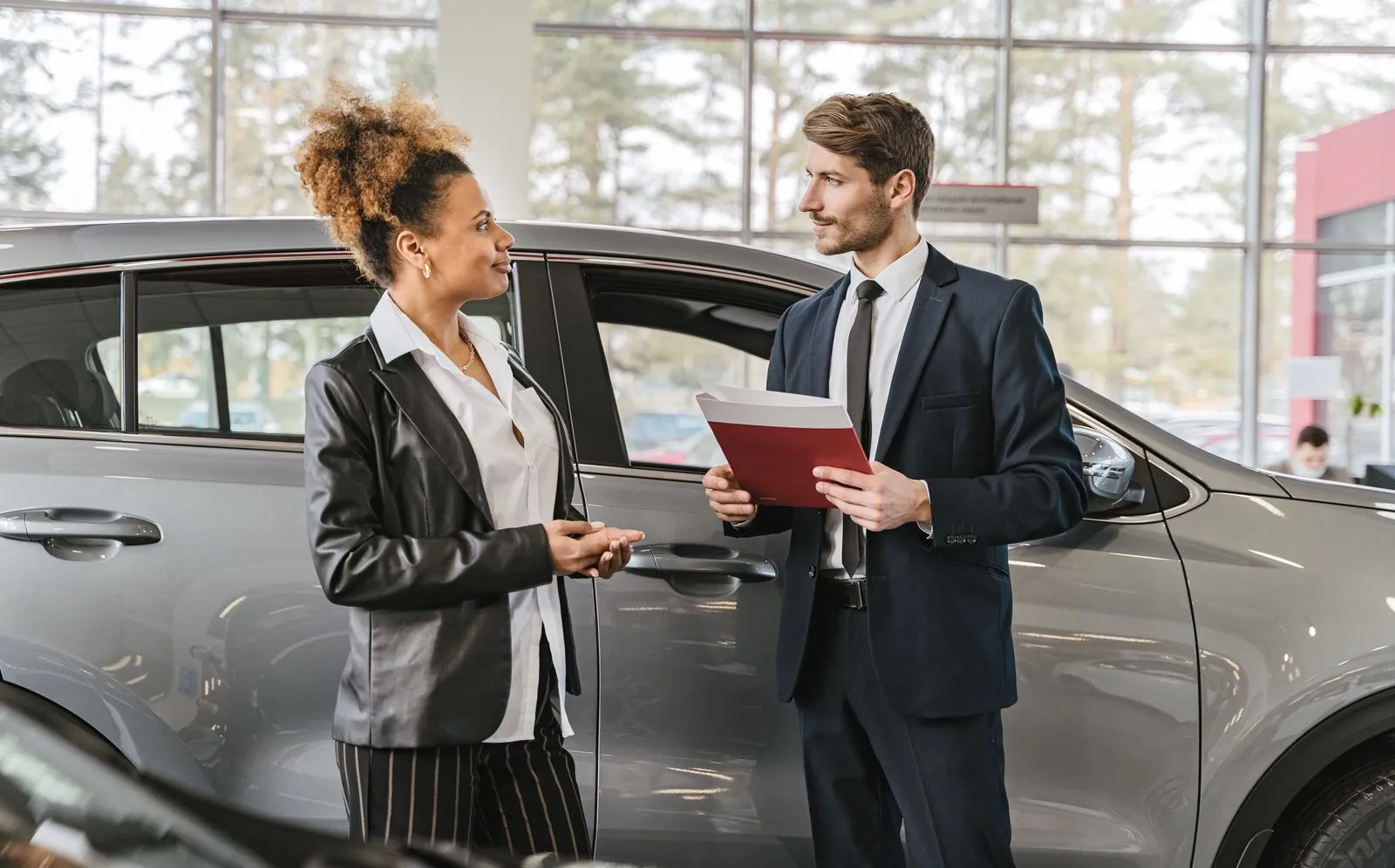 A customer talking with a salesperson at a desk inside a car dealership showroom