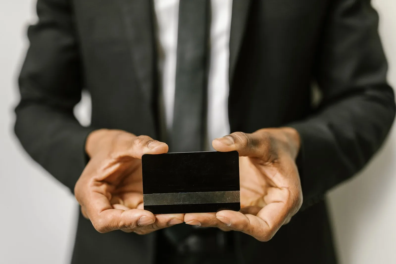 A person in a dark suit holding out a plain black card with no markings on it