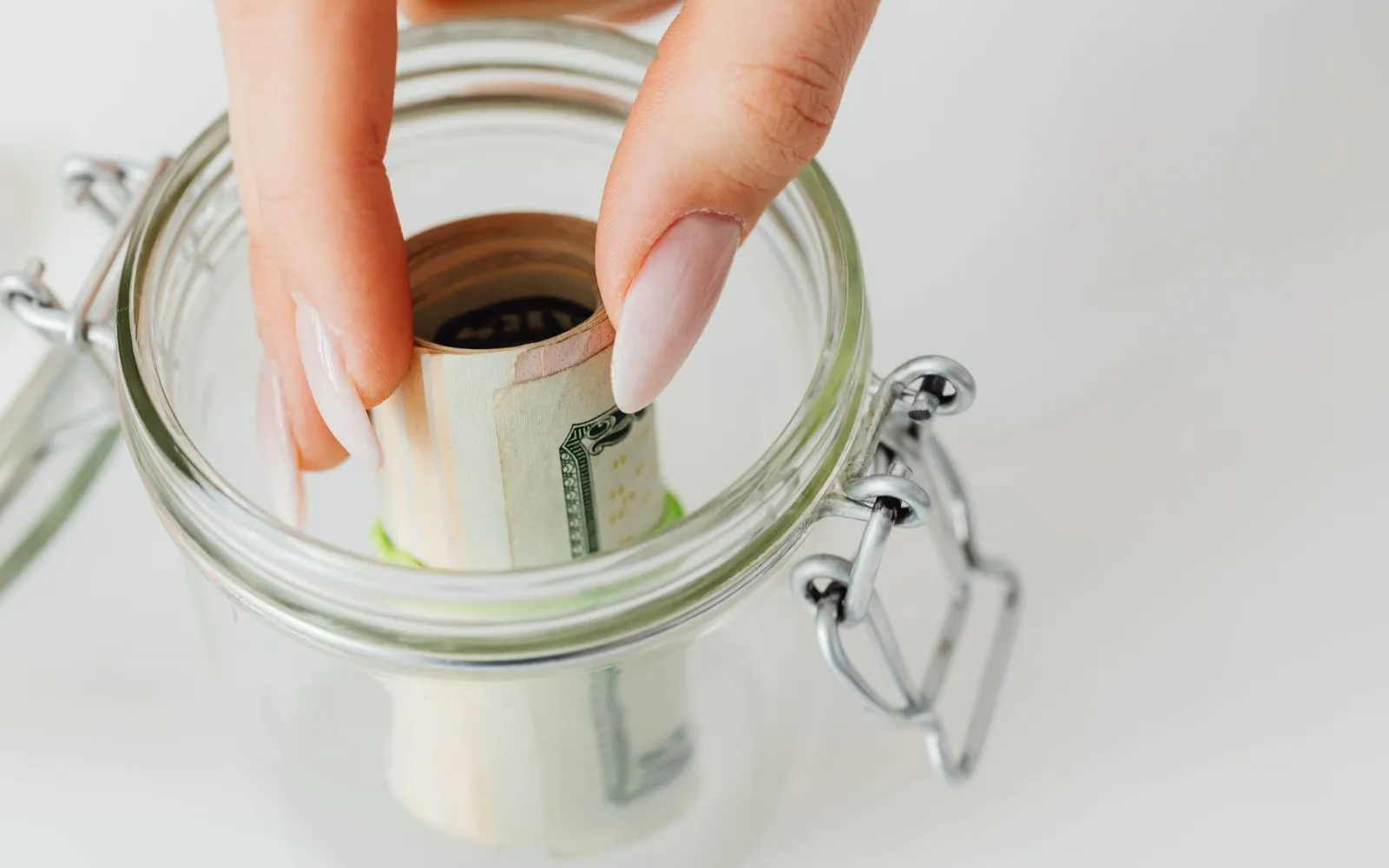 Hand placing a roll of dollar bills into a glass jar with a metal clasp lid