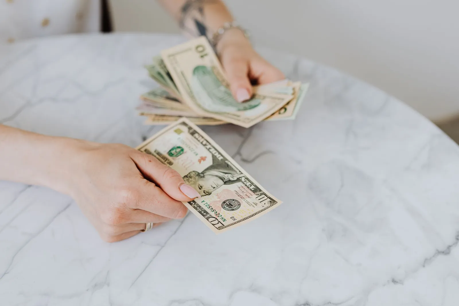 Hands counting ten-dollar bills over a white marble table