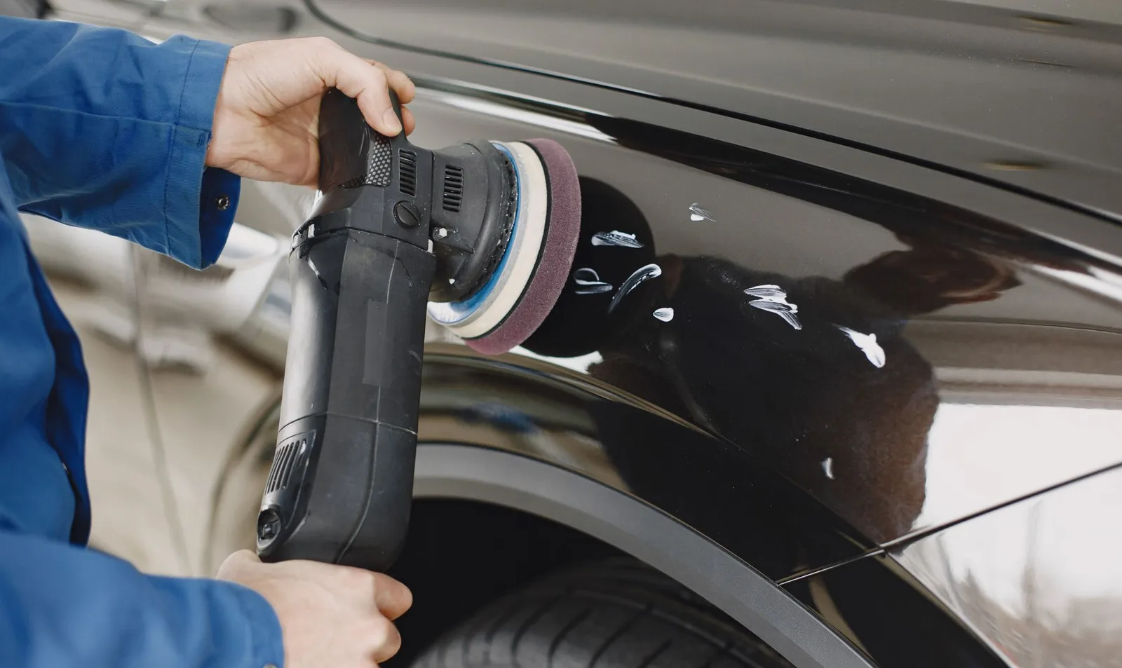 Mechanic in blue coveralls polishing the panel of a black car in a body shop