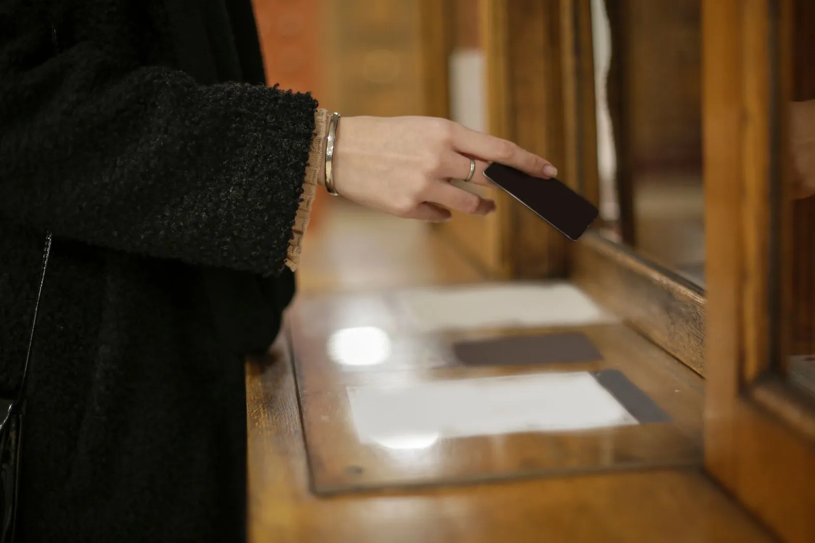 Hand holding a plain black payment card over a wooden counter