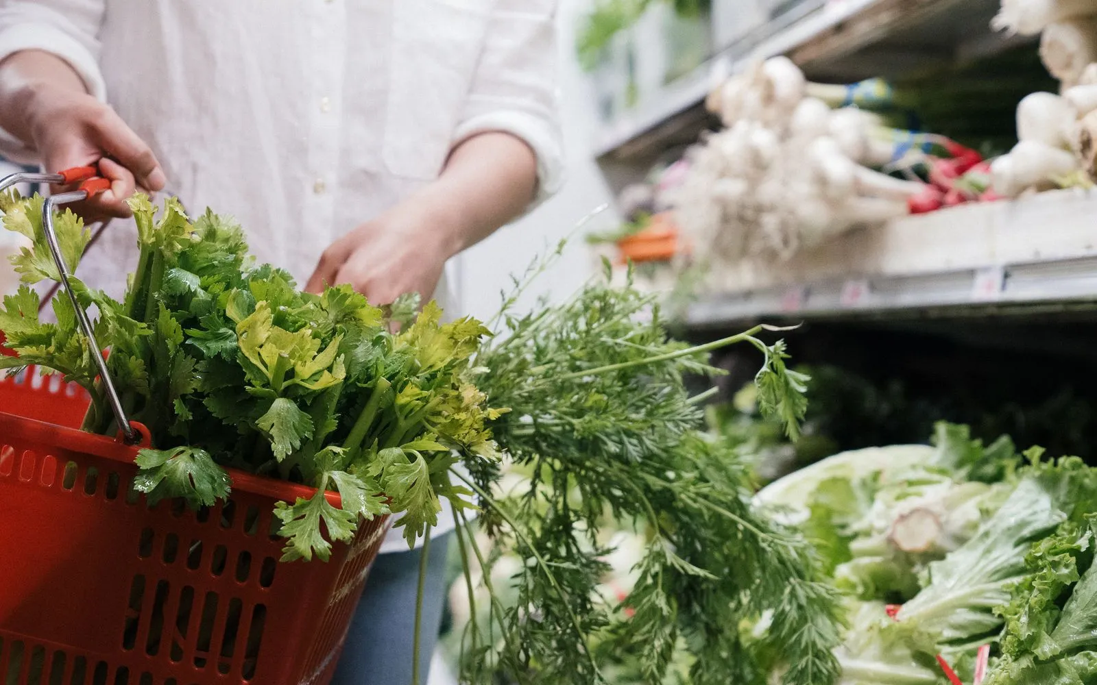 Shopper holding a red basket of fresh greens in a store produce aisle
