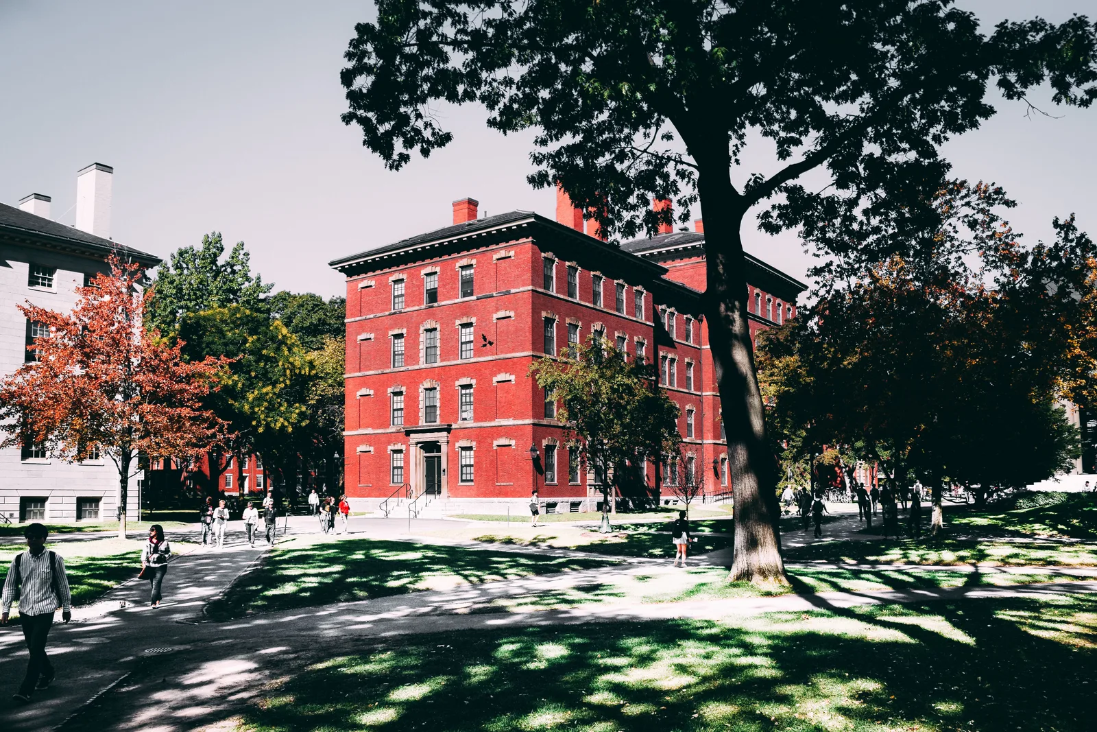 Students walking past a red brick college building on a campus lawn in early fall