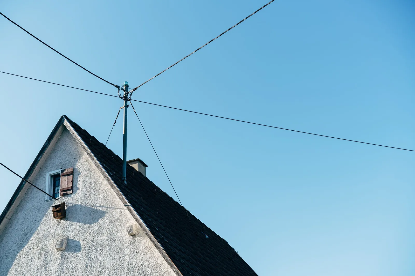 Suburban house rooftop with power lines against a clear blue sky