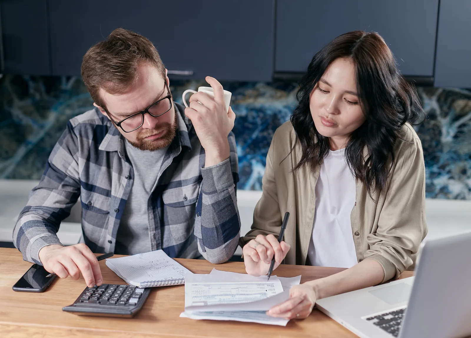 Couple reviewing household bills with a calculator and laptop at home