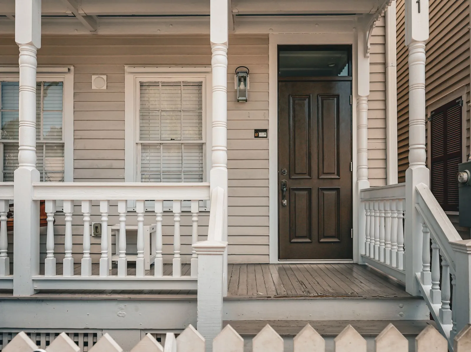 Covered front porch of a clapboard house with a dark wooden front door