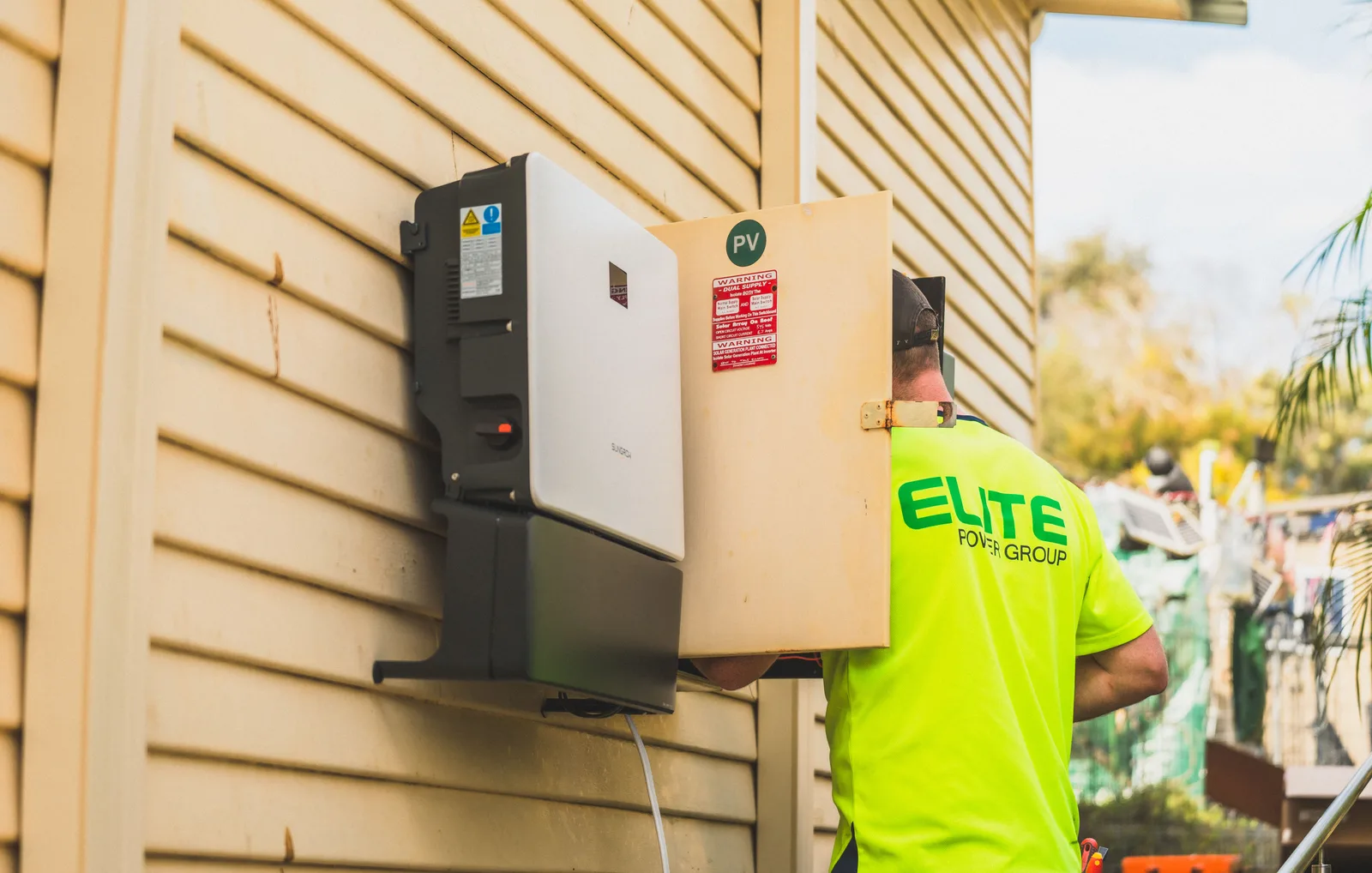 Electrician installing a solar inverter on the outside wall of a house