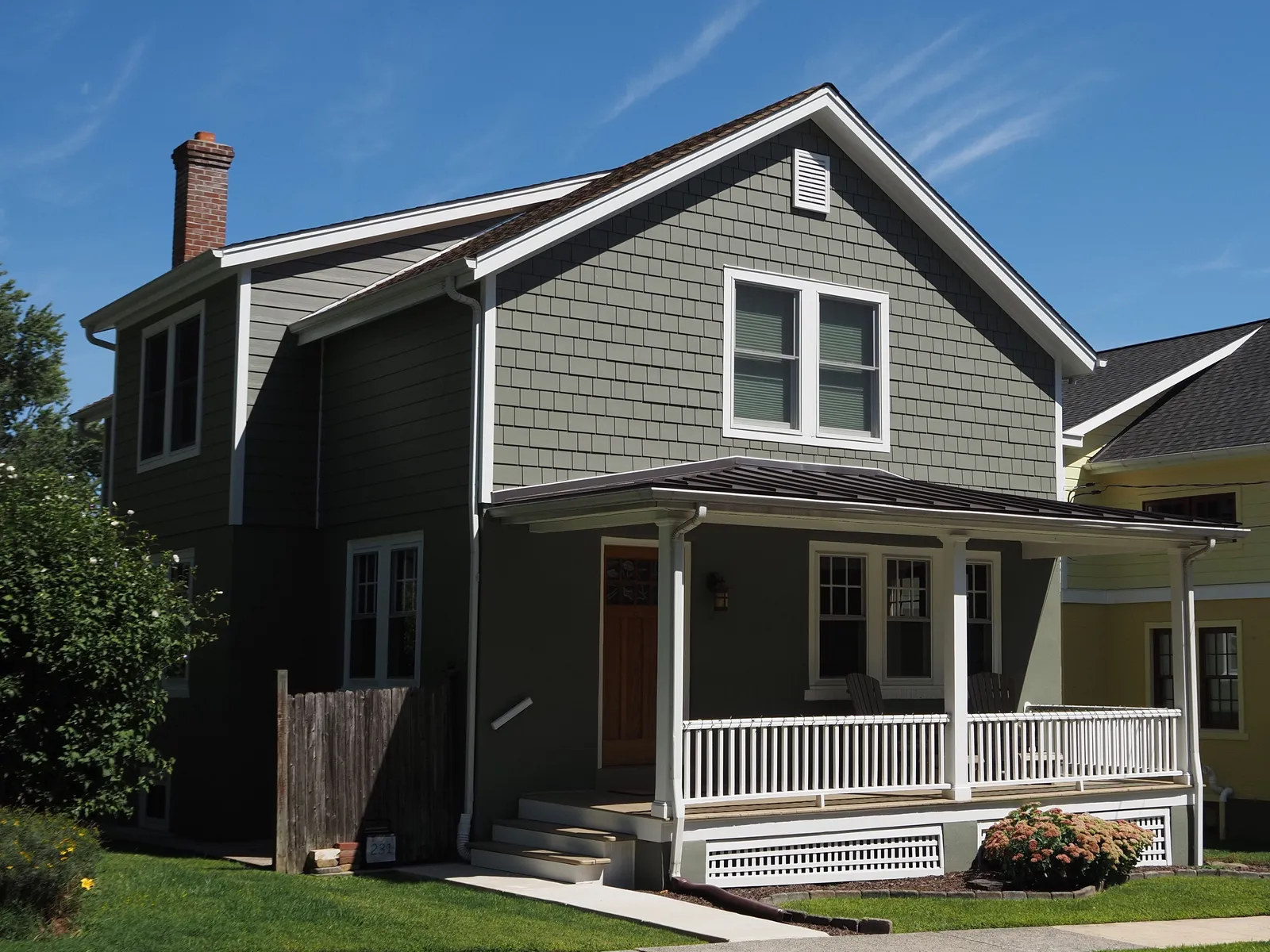 Two-story American house with a covered front porch and white railings on a clear day