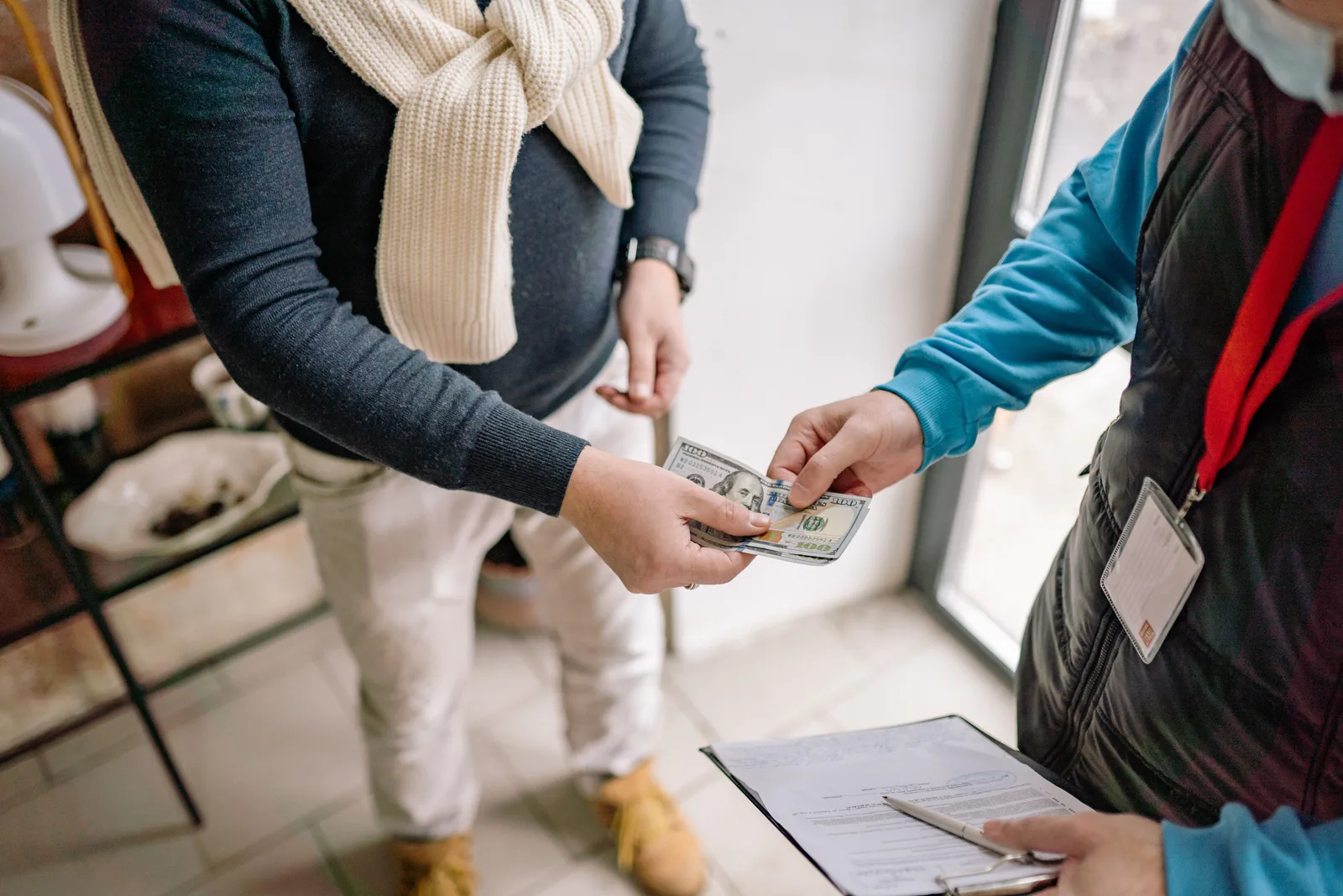 Close-up of two people exchanging cash across a counter indoors