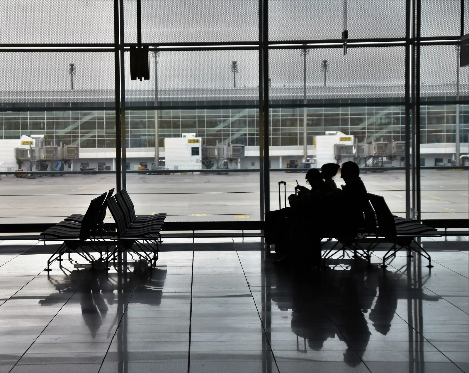 Travelers in silhouette waiting at an airport gate beside a wall of windows