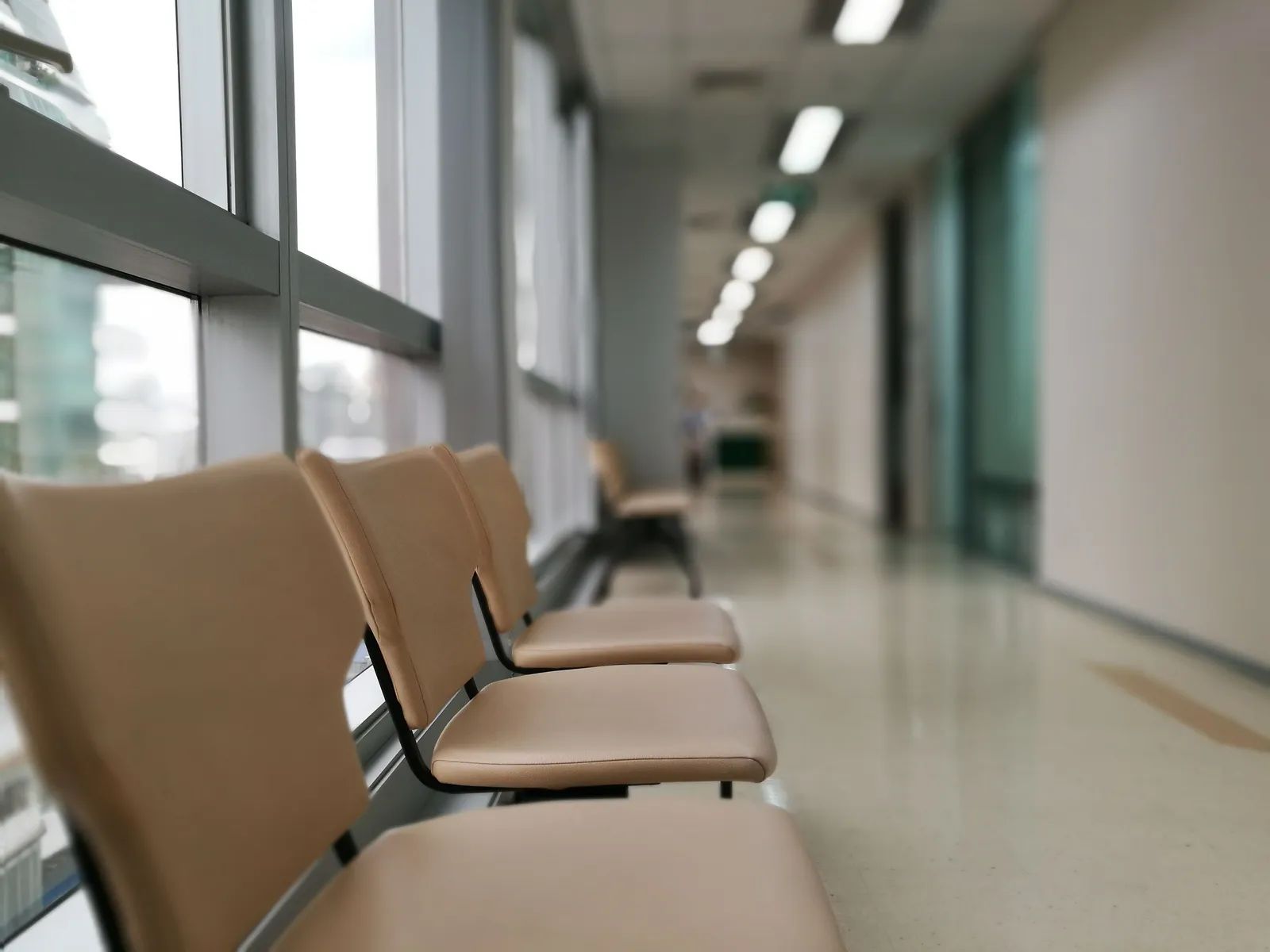 Row of empty tan chairs along the windows of a quiet hospital corridor