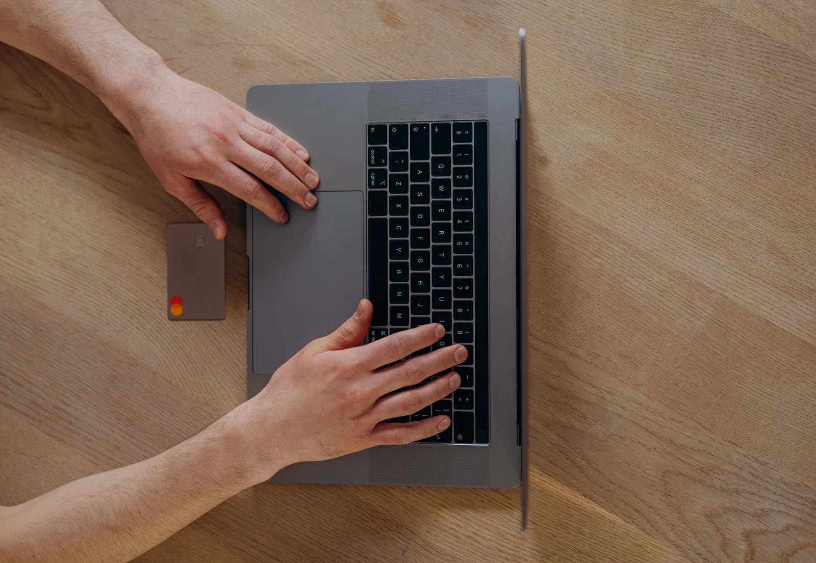 A person using a laptop beside a credit card on a wooden table