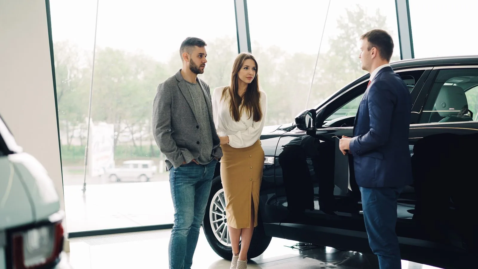 A couple talking with a salesperson beside a car inside a dealership showroom