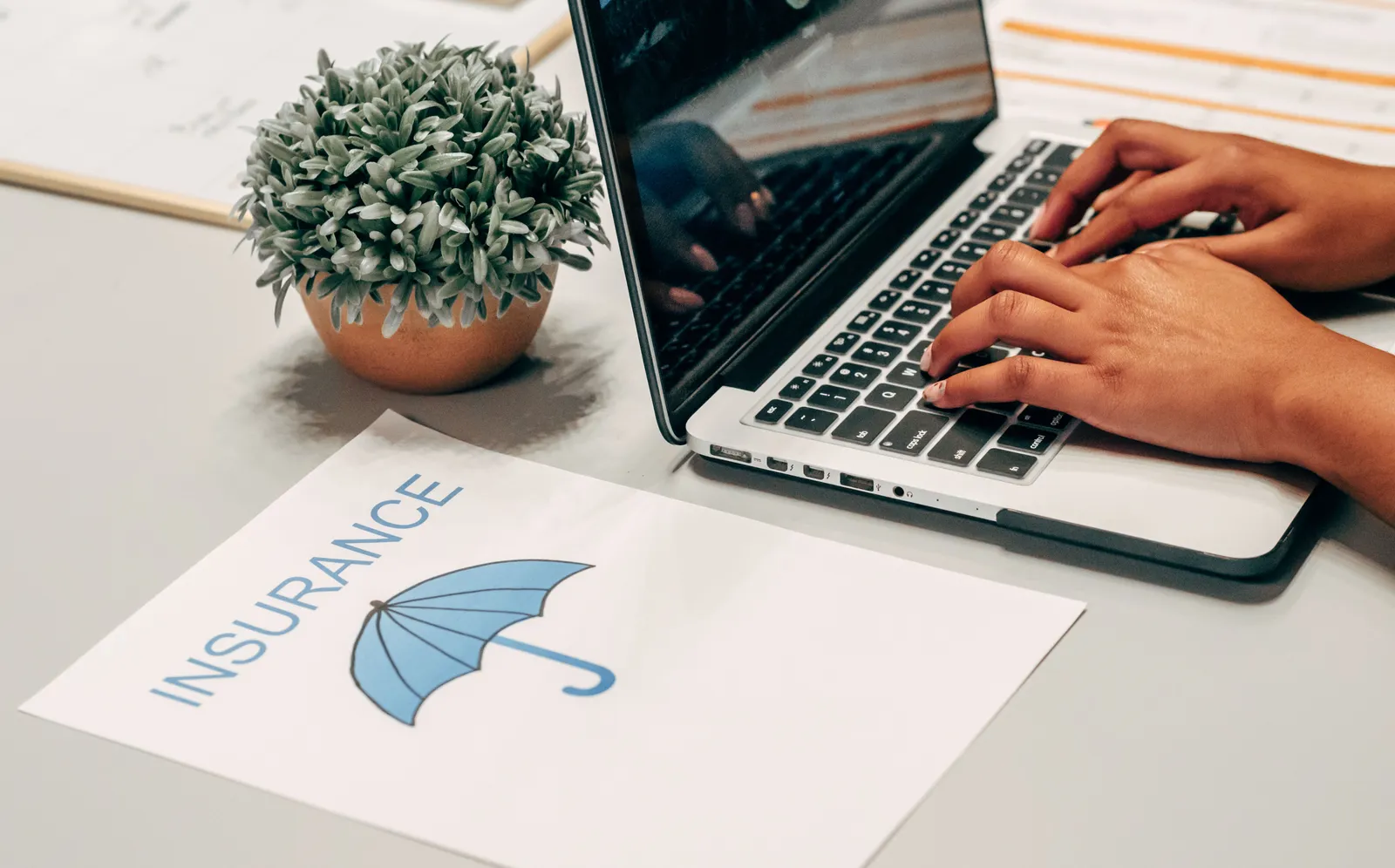 Hands typing on a laptop at a desk next to a printed insurance policy