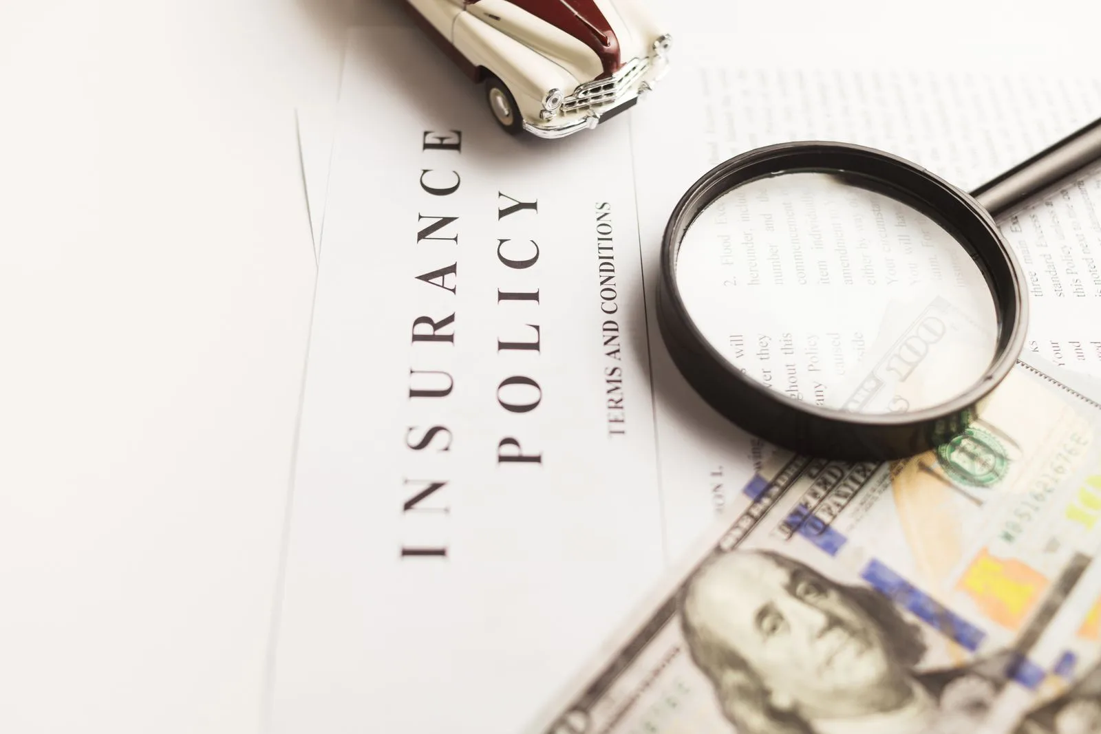 An auto insurance policy document beside a magnifying glass and cash