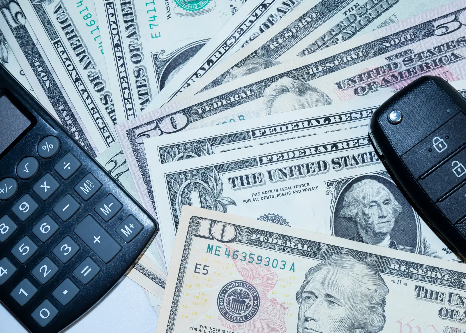 Calculator and a car key fob resting on fanned-out US dollar bills