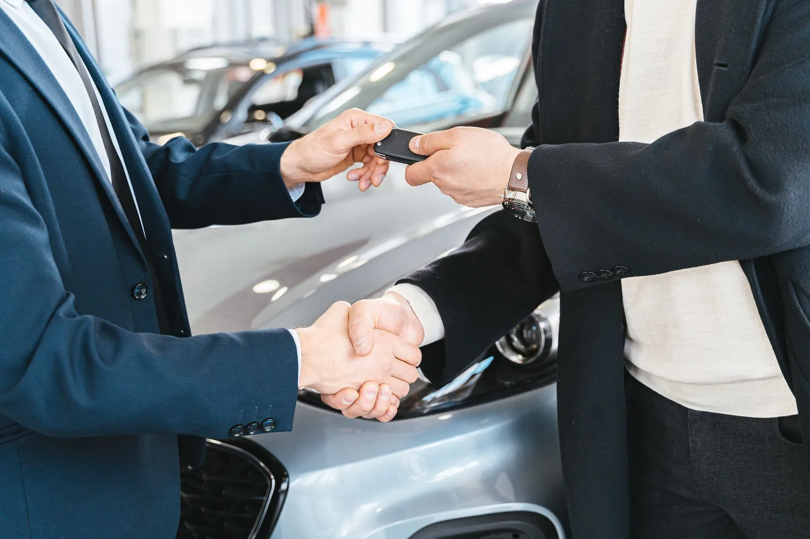 Car salesperson shaking hands with a buyer and handing over a key fob in a dealership showroom