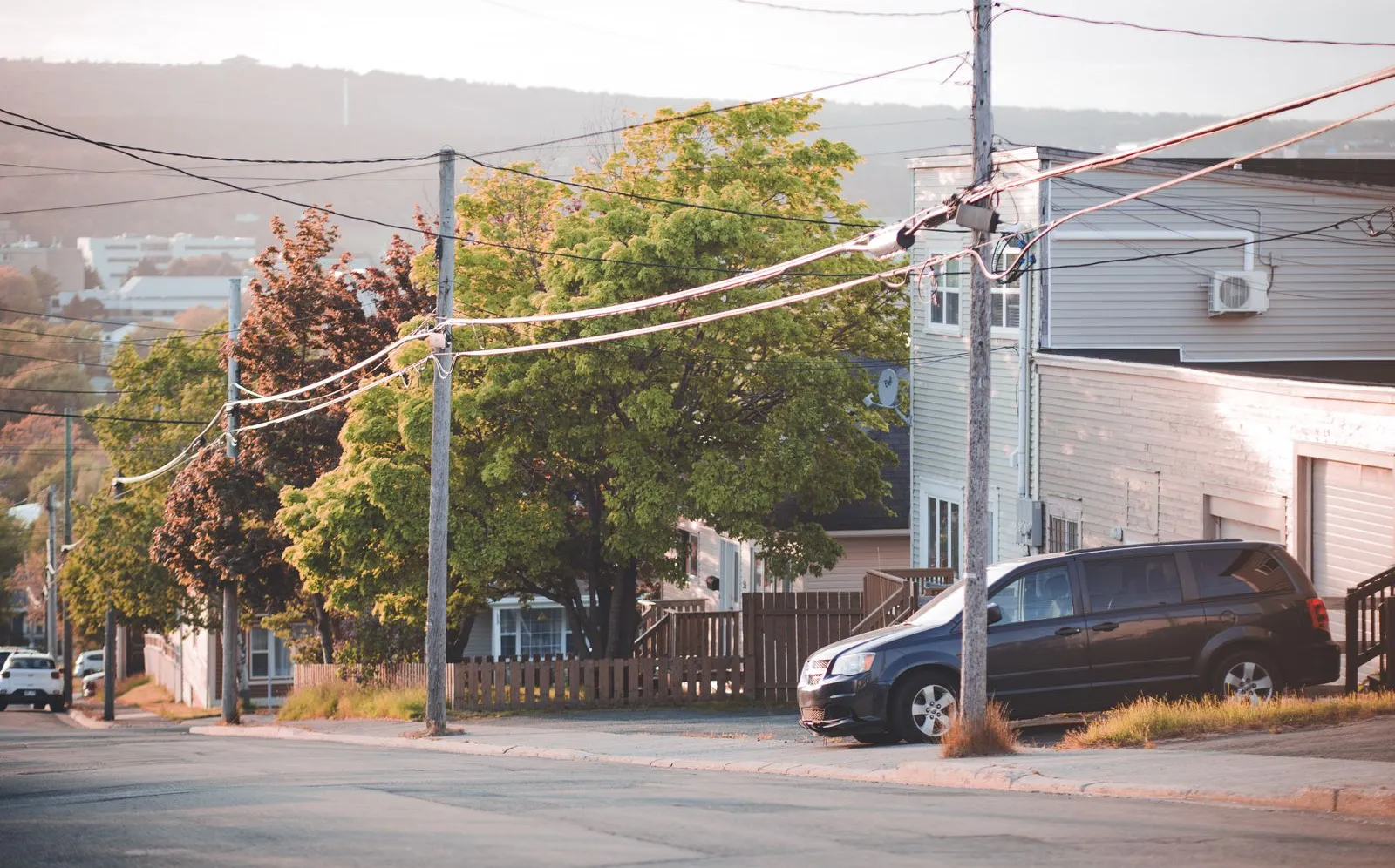 A minivan parked on a quiet residential street lined with houses and trees at sunset
