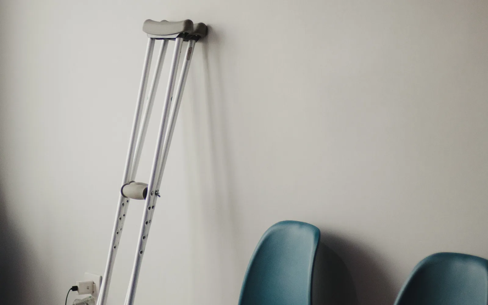 A pair of crutches leaning against a clinic wall beside two empty blue waiting room chairs