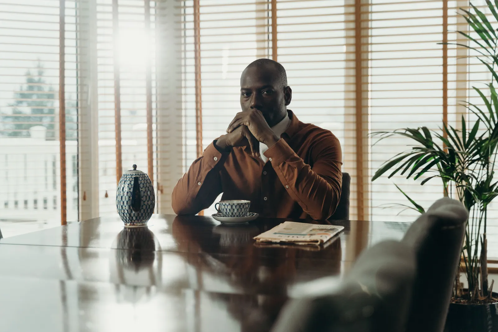 Man sitting alone at a dining table with a cup of coffee, looking toward a sunlit window