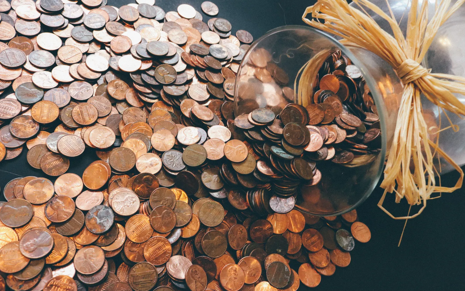 Glass jar tipped on its side with pennies spilling across a dark table