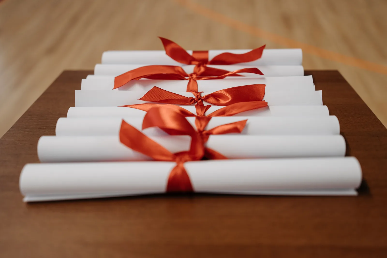 Rolled diplomas tied with red ribbon resting on a wooden desk