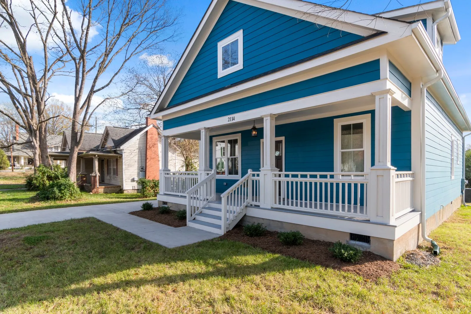 A blue single-family house with a white front porch and a green front lawn on a clear day