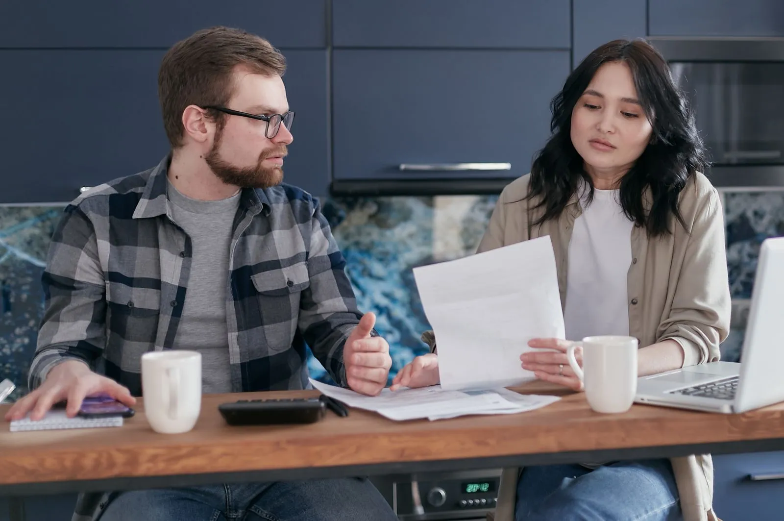 Two adults at a kitchen table going over a bill with a calculator and laptop