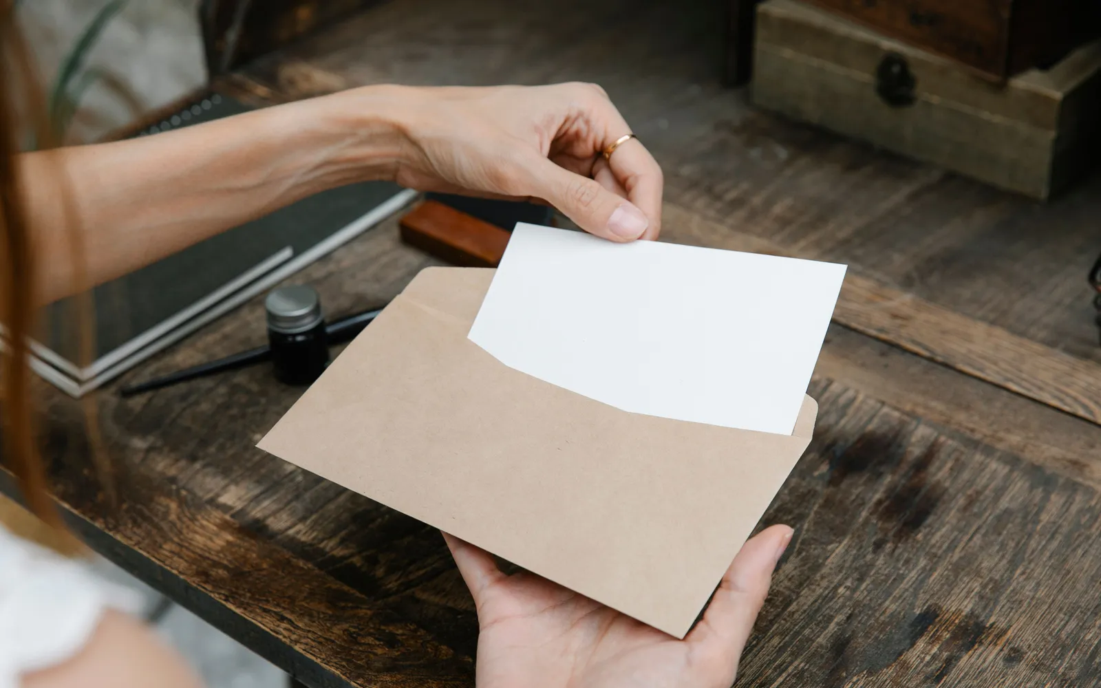 Close-up of hands taking a letter out of an envelope on a wooden desk