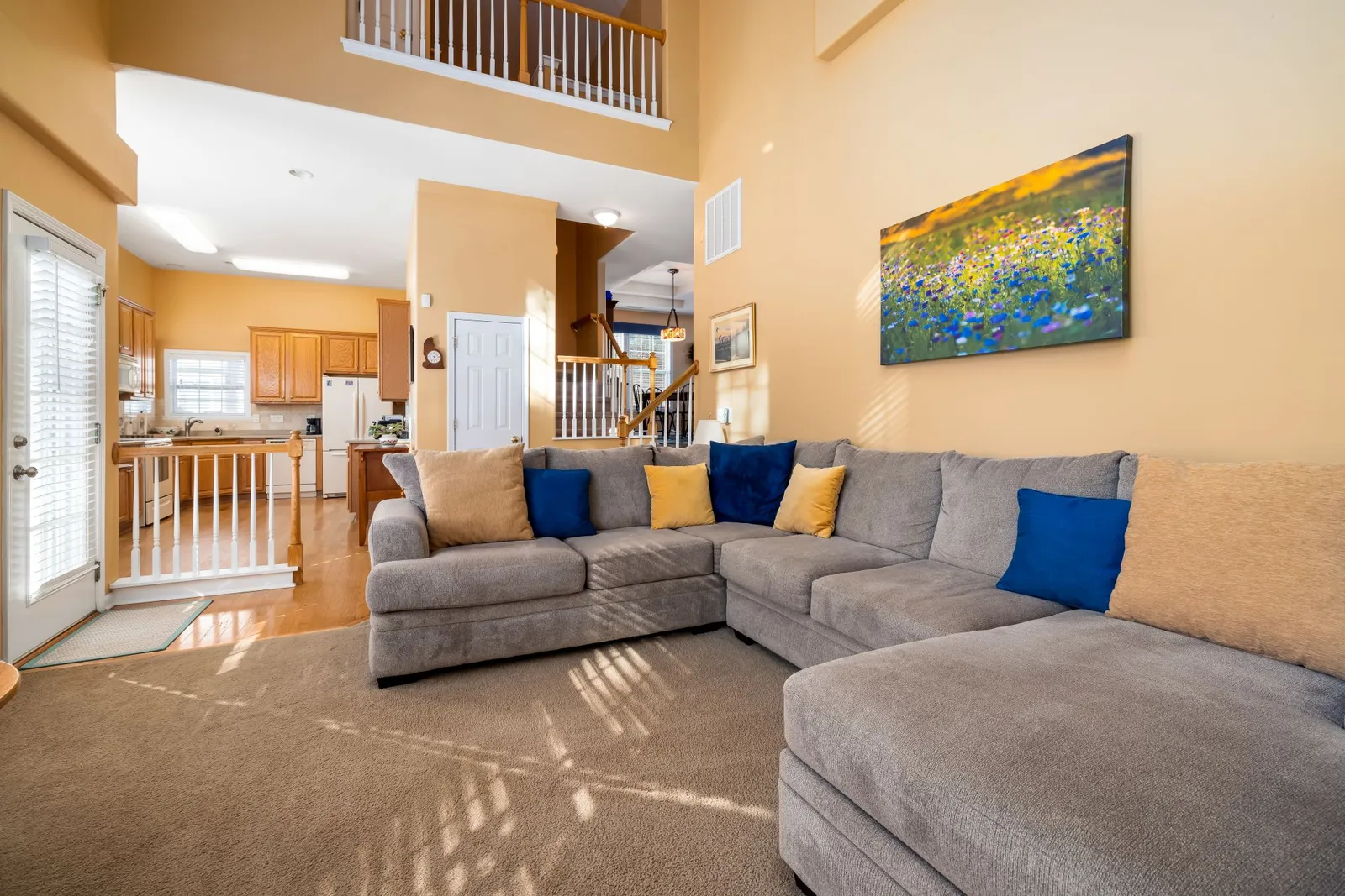 Gray sectional sofa with blue and yellow pillows in a carpeted two-story living room