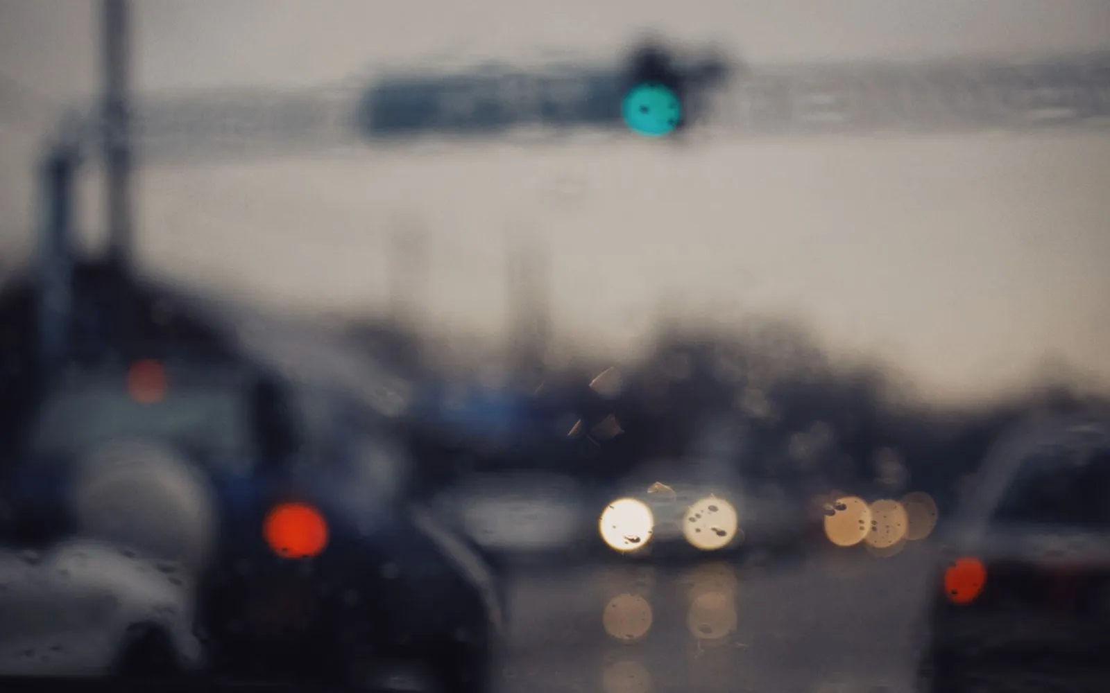 Blurred traffic and headlights seen through a rain-streaked windshield at dusk