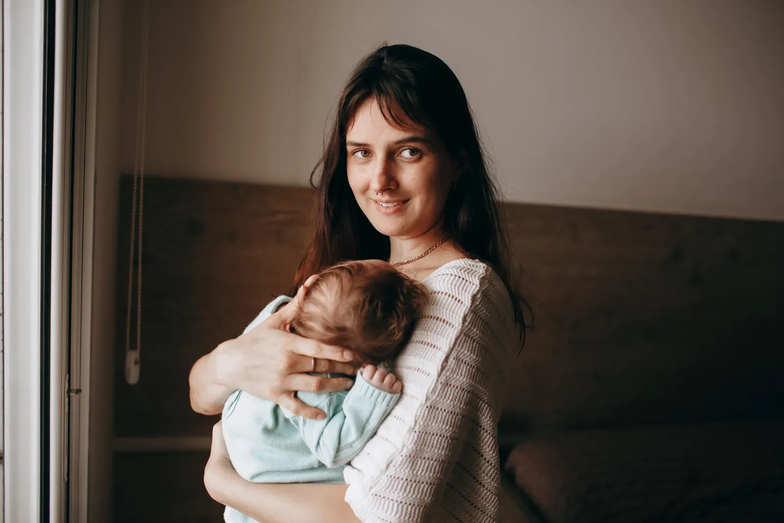 Mother holding her sleeping newborn by a window at home