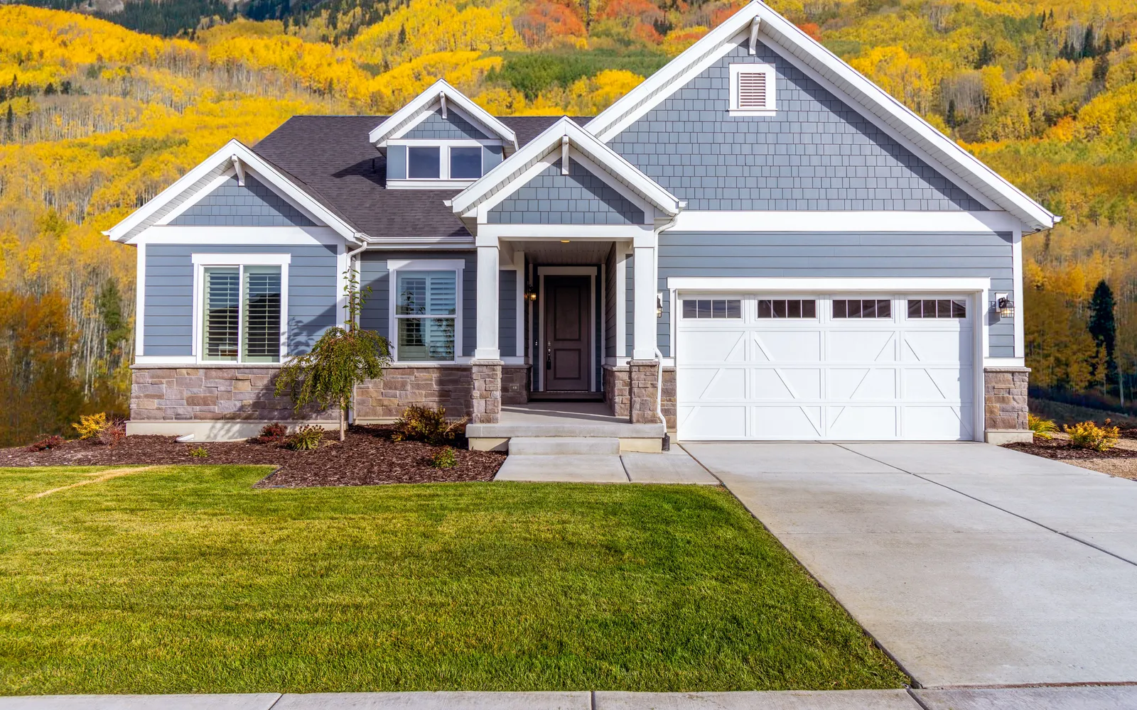 Gray craftsman-style house with a white two-car garage and a new lawn, with hills of yellow fall aspens behind it