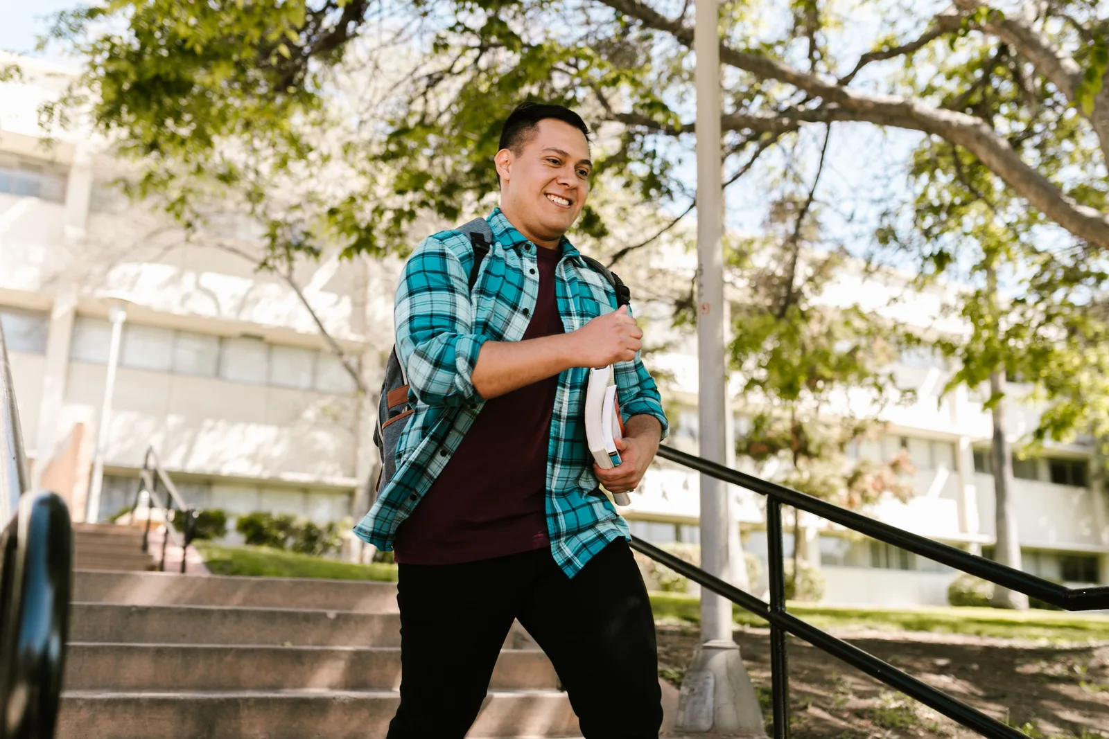 College student carrying books walking down campus steps on a sunny day