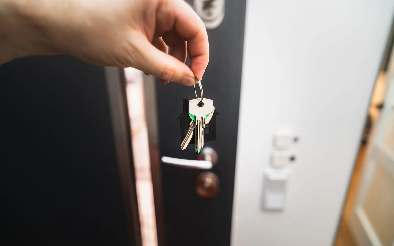 Hand holding a set of house keys in front of an open front door