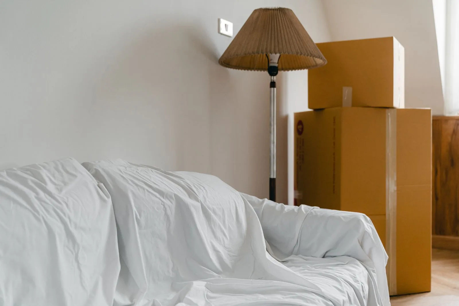 Packed cardboard boxes and a sheet-covered sofa in a room being emptied