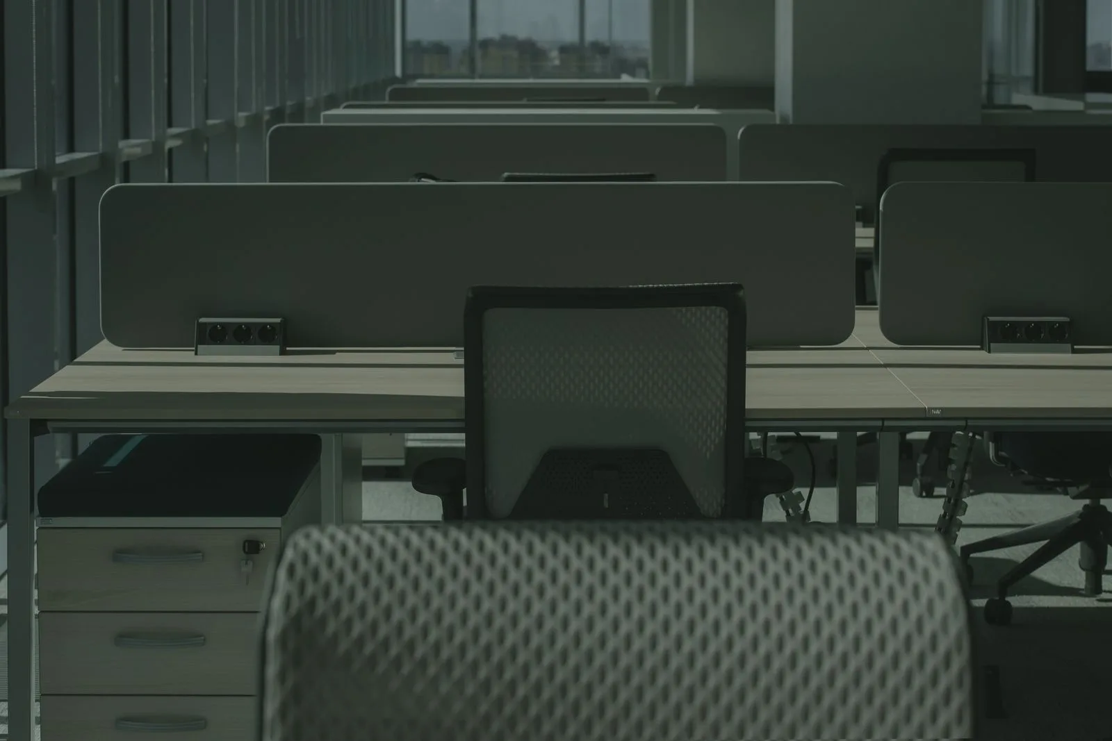 Rows of empty desks and vacant chairs in a dim open-plan office