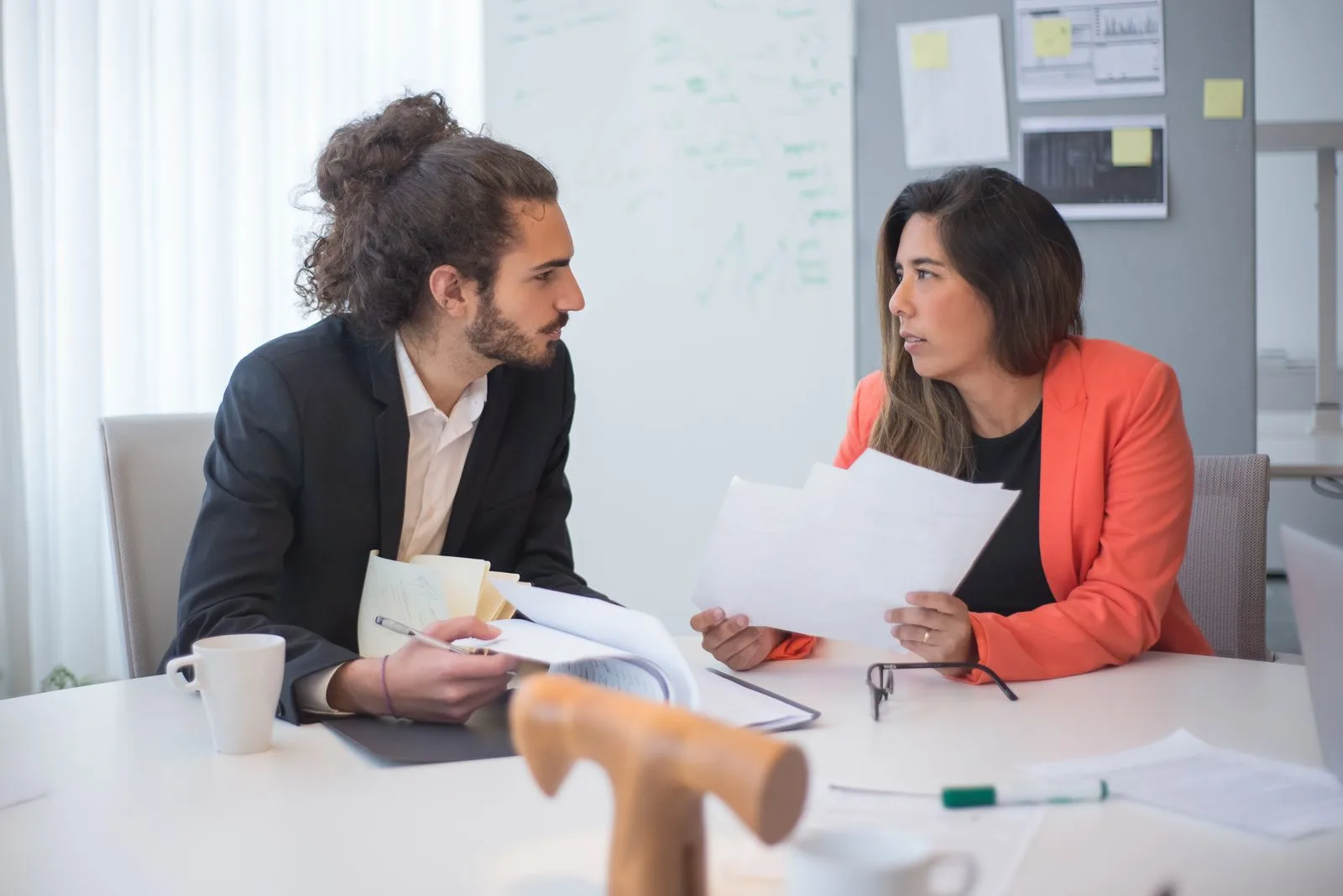 Two people at an office table looking at each other across a spread of paperwork